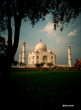 The Taj Mahal, a white marble mausoleum, stands against a cloudy sky.