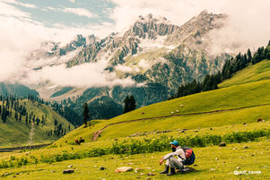 Person sitting on green grass looking at the beautiful mountains in Kashmir.