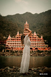 Woman in white dress poses near temple and river against mountain backdrop