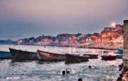 Boats float on water near city buildings at dusk. Indian Wildlife Tour With Temples.