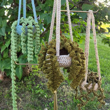Three different crocheted hanging plants hang on hooks outside.