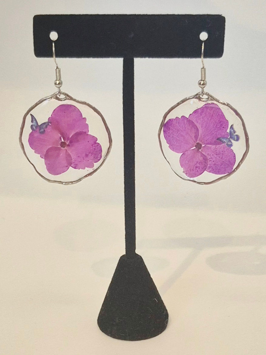 Thumbnail: A pair of lightweight, handmade resin earrings featuring purple flowers and a delicate butterfly accent