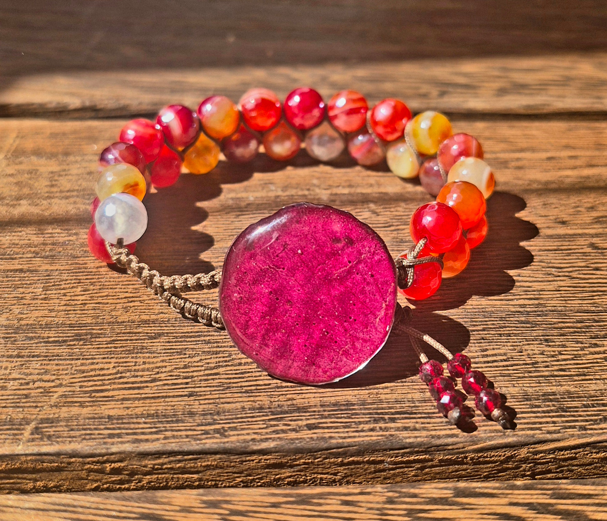 A full view of a handmade bracelet with faceted red and orange agate beads, featuring a rose petal resin button clasp