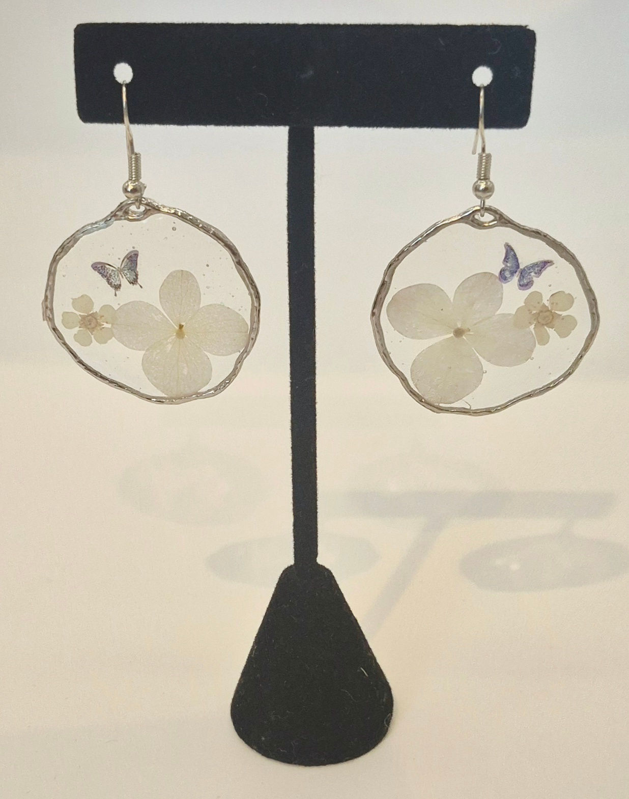 A pair of lightweight, handmade resin earrings featuring white flowers and a delicate butterfly accent