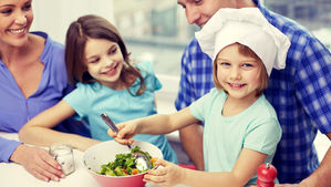 A little girl mixing a salad with her family around her.
