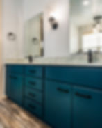 Blue bathroom vanity with black handles, marble countertop, two mirrors, and wall lights. Wood floor adds warmth to a clean setting.