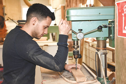David Payet, Tischlermeister, konzentriert bei der Arbeit in seiner Werkstatt – mit Holz und Werkzeug in der Hand.