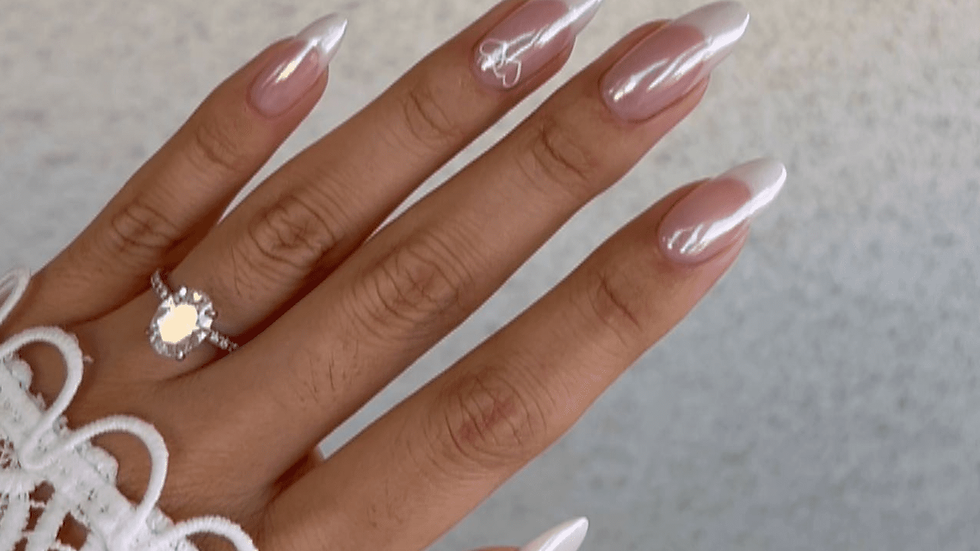 Hand with long, pink-to-white gradient nails and a diamond ring against a light background. Lace sleeve adds elegance.