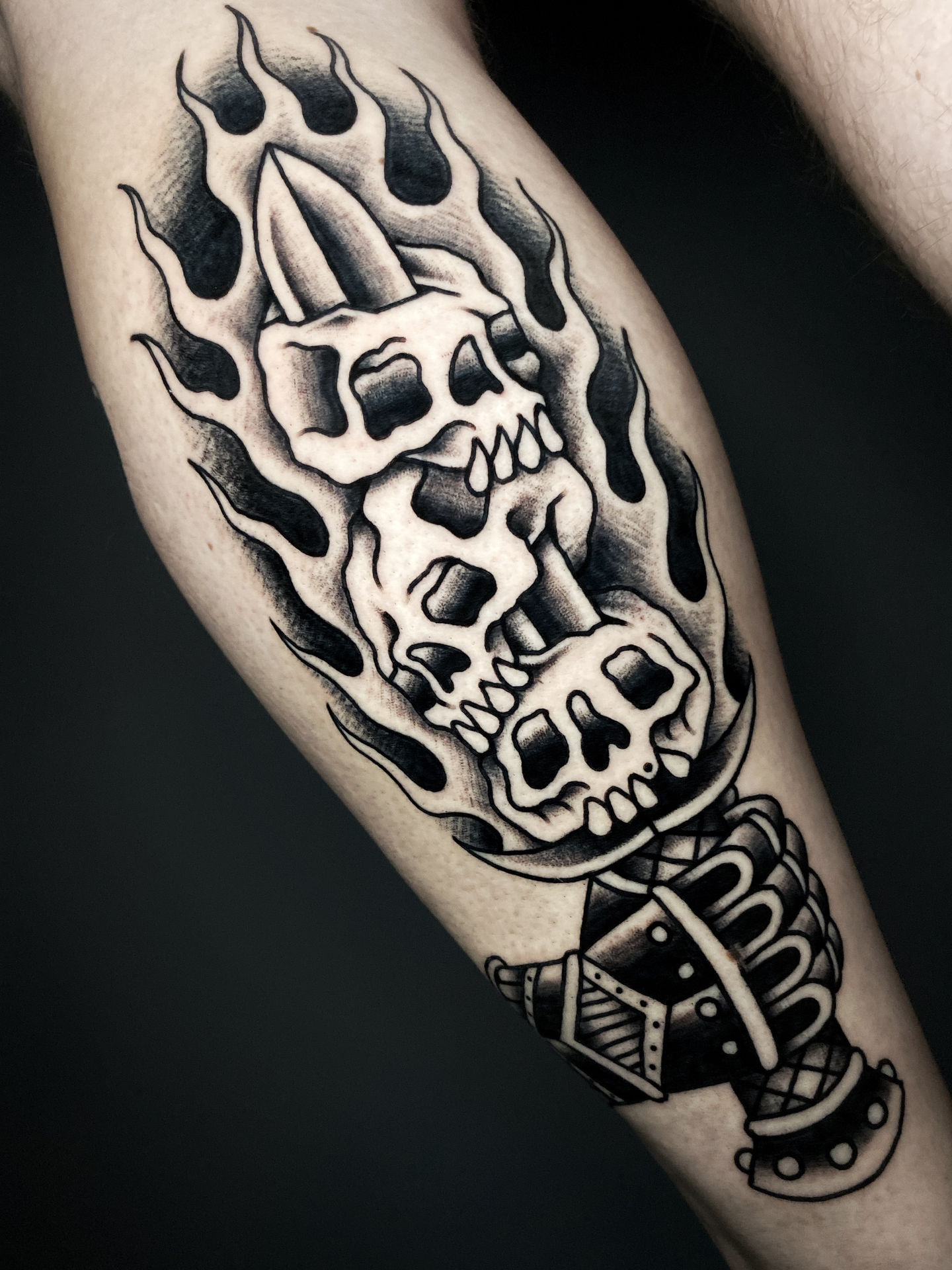 traditional american tattoo of medieval gauntlet holding sword with skulls and fire