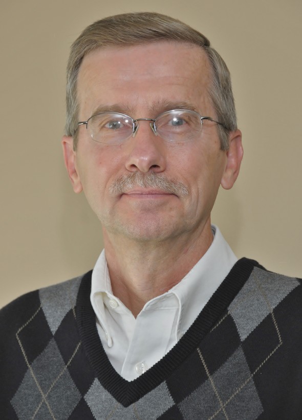 Professional headshot of a man with glasses and sweater.