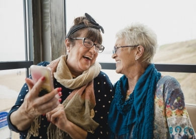 Two senior women laughing while looking at a smartphone.