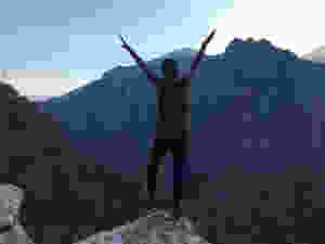 Kelly standing in front of a mountain, arms raised.