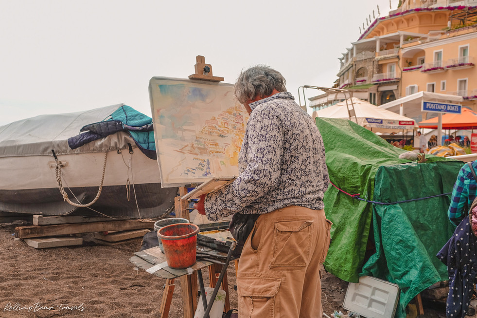 An artist painting on an easel by the beach of Positano | RollingBear Travels.