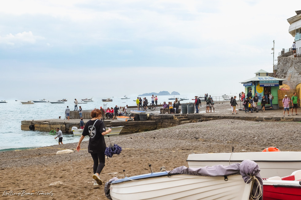 A girl walking down the beach of Positano towards the pier | RollingBear Travels.