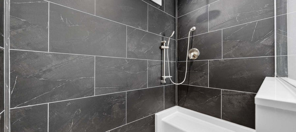 Modern shower with dark slate tiles and a white bench seat.