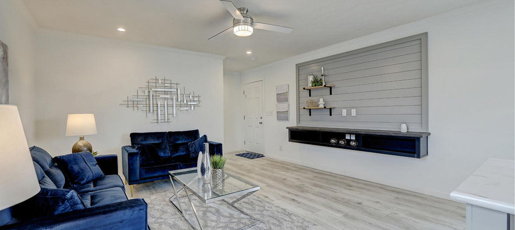 Modern living room with blue sofas, glass table, and wall bar