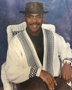 a man wearing a hat and glasses is sitting in a wicker chair ~ Dwayne Stoutamire