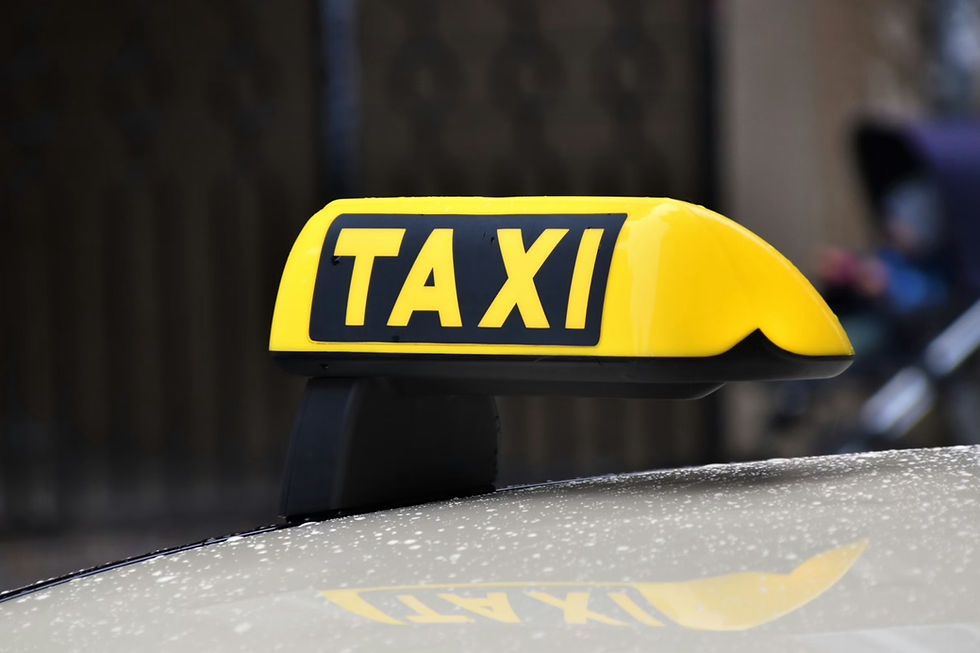 Yellow taxi sign on car roof with raindrops, bold black "TAXI" text. Blurred background, rainy day.