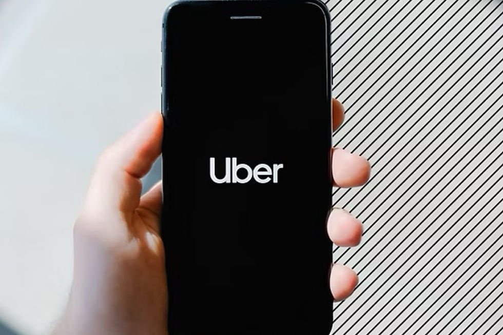 Hand holding a smartphone displaying the Uber logo on a black screen. Background features diagonal black and white stripes.