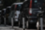 Taxis are parked closely on a taxi rank alongside a street with metal bollards. The scene is urban, featuring black and silver vehicles.
