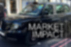 Black taxi on city street with "MARKET IMPACT" text overlay. Background shows storefronts and a pedestrian. Bright daylight.