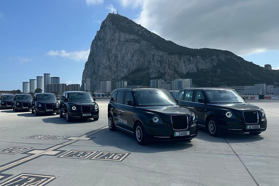 Black LEVC taxis parked on a tarmac with The Rock of Gibraltar in the background. Clear sky with some clouds. Taxis have visible license plates.