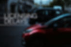 Red and black cars on a city street with pedestrians. Text reads "LICENSING DELAYS." Overcast sky and muted colors create a somber mood.