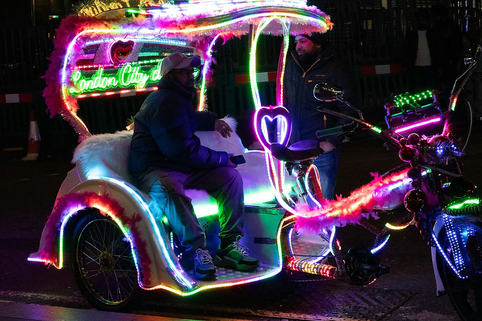 Two men with a neon-lit rickshaw, decorated with colorful lights and "London City" sign, create a vibrant scene at night.