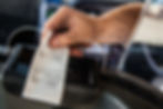Hand holding a taxi receipt through a partition inside a vehicle. Text and details visible on the receipt; mood is neutral and transactional.