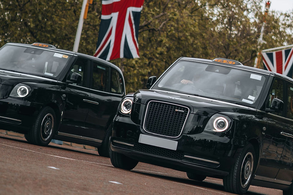 Black taxis driving past a Union Jack flag. The scene is set outdoors with trees and an overcast mood. "TAXI" signs visible.