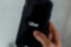Hand holding a smartphone displaying the Uber logo on a black screen. The background is blurred and gray, creating a focused, modern feel.