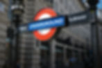 Red and blue London Underground sign reading "PUBLIC SUBWAY" against a busy city street background with historic stone buildings.