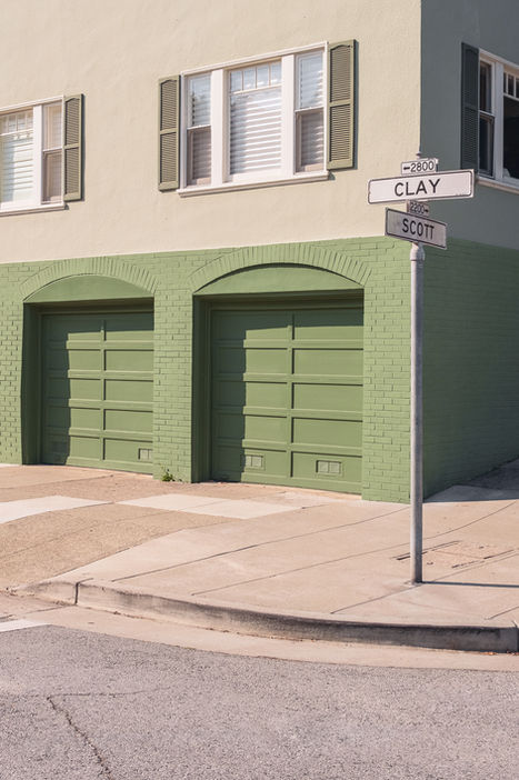 Light green building with two green garage doors and Clay street sign