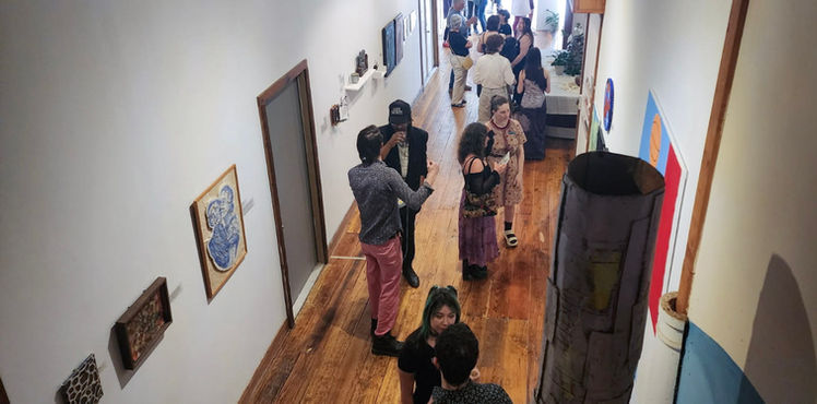 A group of participants during the open reception of ARCHIVES Boundaries engage in conversation in a hallway surrounded by artwork. The hallway extends back to show a gathering of people engaged in talking about the artwork on the walls.