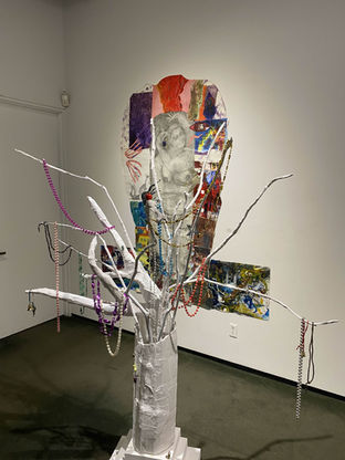 A tree made of cardboard, plaster, gathered sticks and mardi gras beads in an art gallery