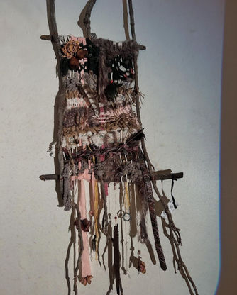 A weaving art piece made of found fabrics and objects. Earth tones with pink highlights
