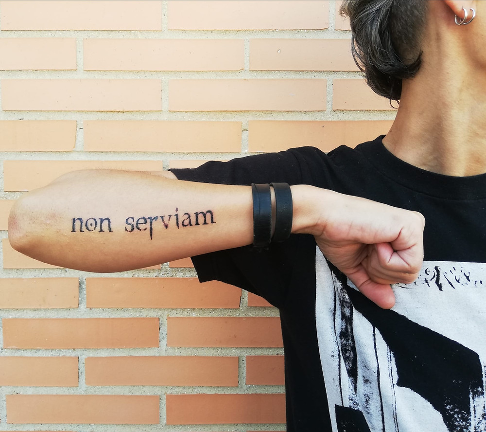 Tattoo on an arm saying the latin phrase non serviam