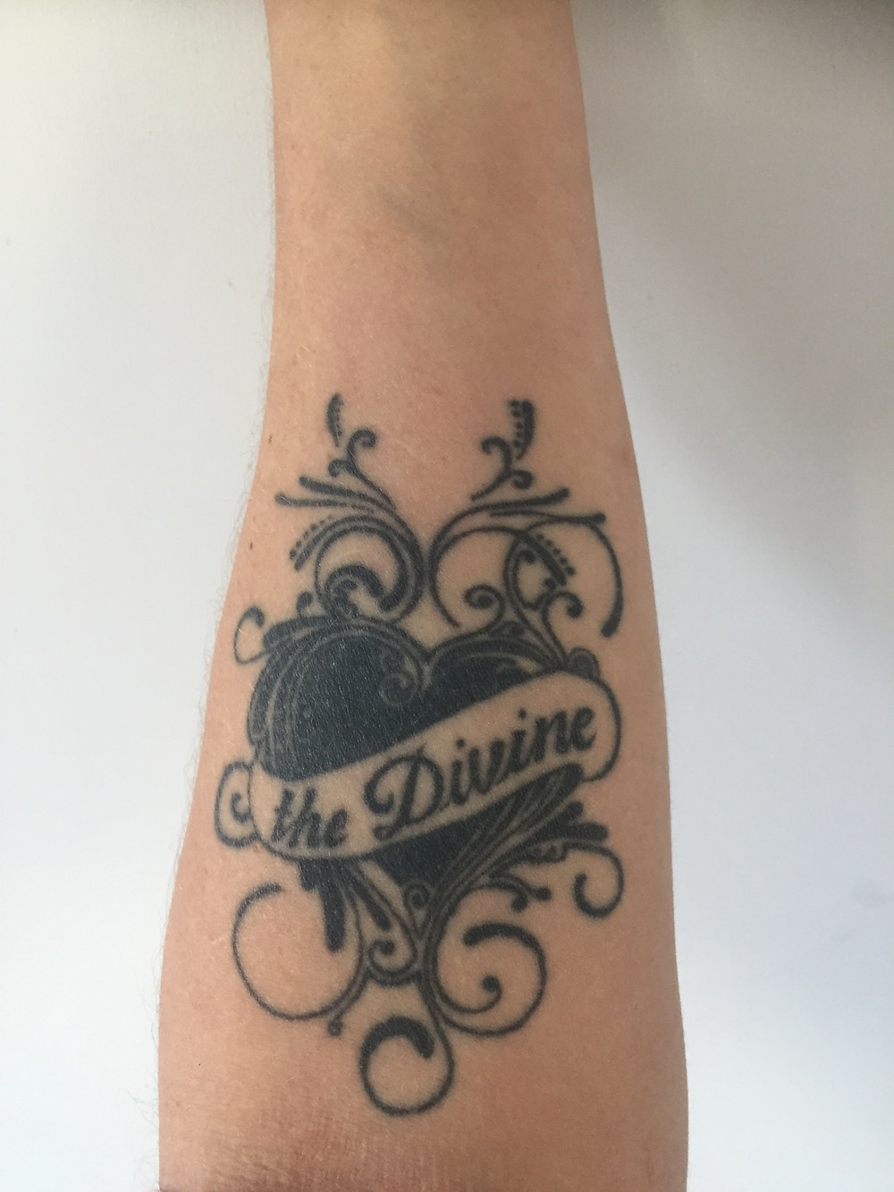 Tattoo on an arm of a heart with the word divine written inside it