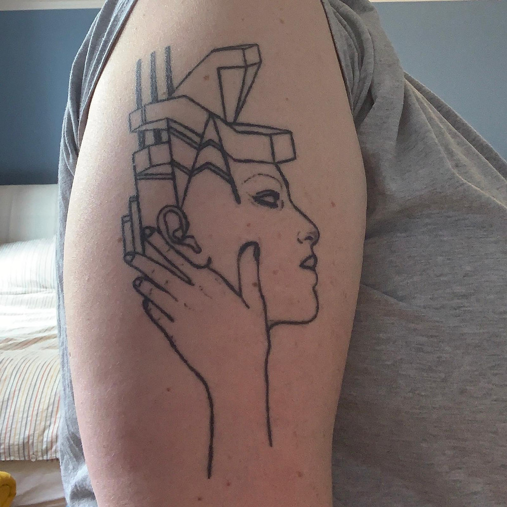 Tattoo on an arm of a face coming out of a building