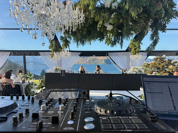View from the DJ decks through a chandelier-lit marquee and bar toward the lake and mountains.