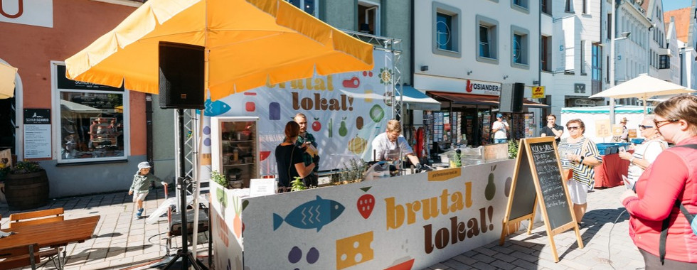 Essen wird an einem Stand ausgegeben, zwei Mitarbeiter stehen hinter der Theke.