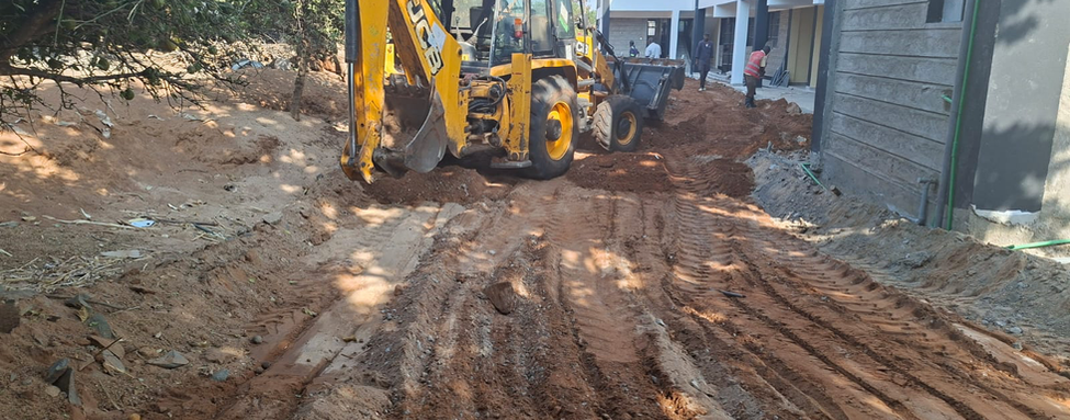 Yellow backhoe grading red soil beside the school building under construction
