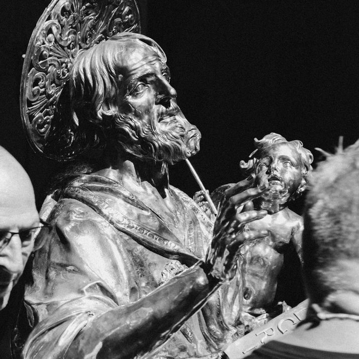Black and white close-up of a silver statue of a saint surrounded by men helping to move or install it.