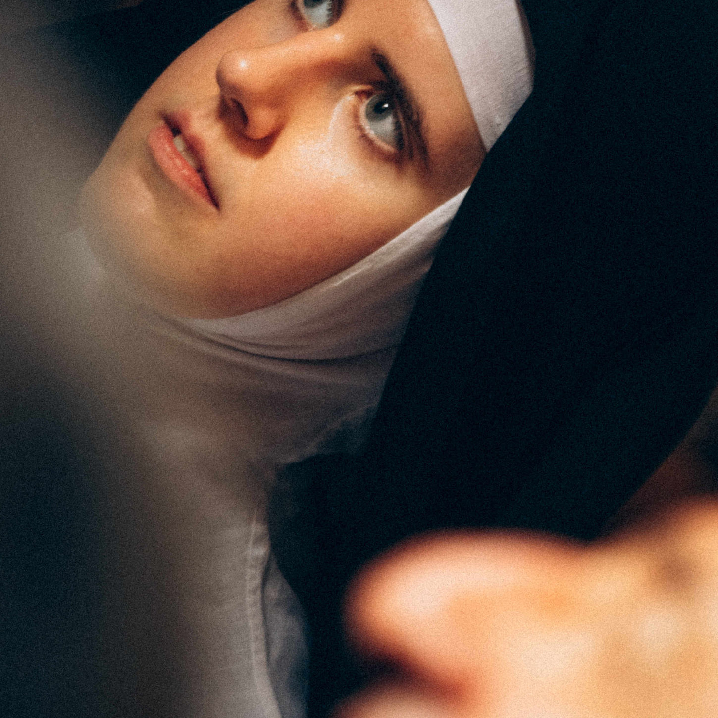 Close-up portrait of a young nun wearing a traditional white and black habit, looking upwards with a solemn expression.