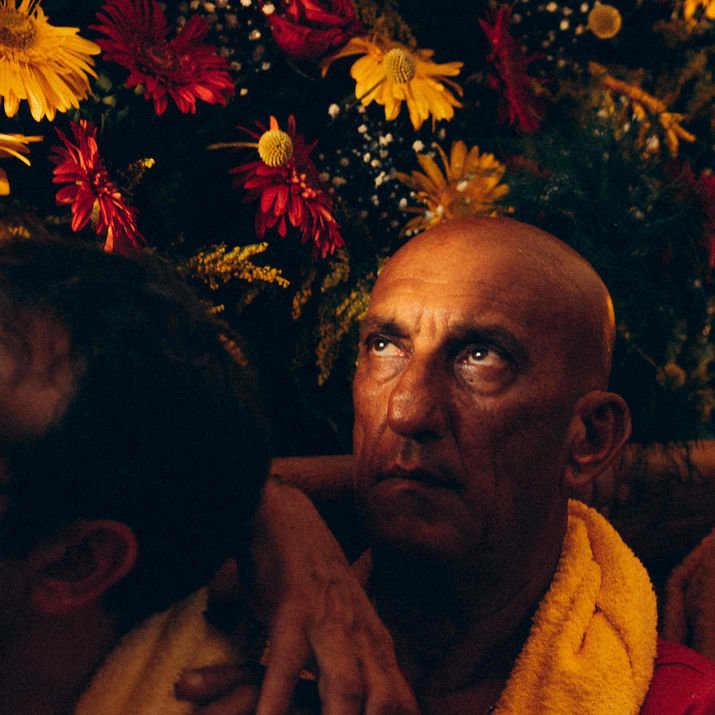 Vertical close-up of a man with an intense gaze framed by colorful flowers during a religious festivity.