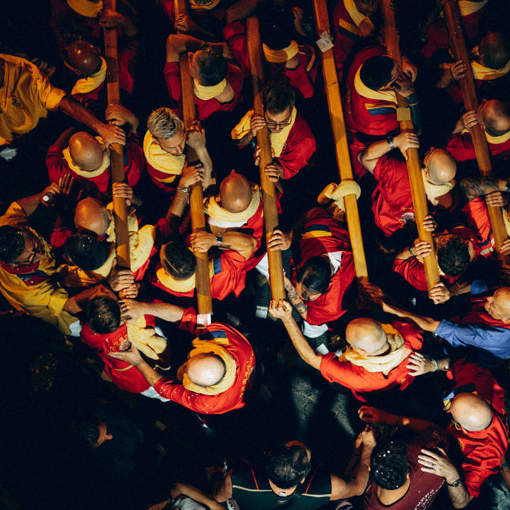 High-angle overhead view of bearers in traditional red and yellow garments holding wooden poles during a religious procession.