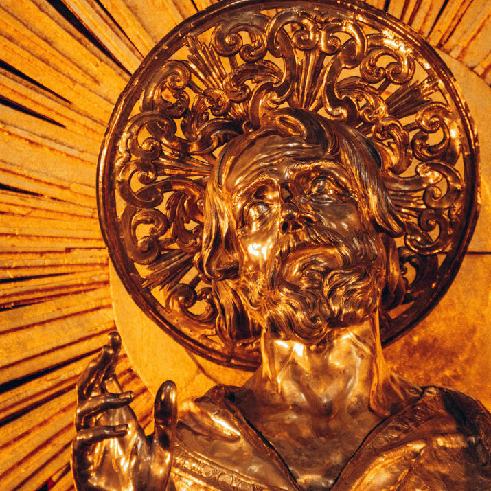 Close-up of a golden religious statue illuminated with a radiant halo, showcasing intricate carved details.