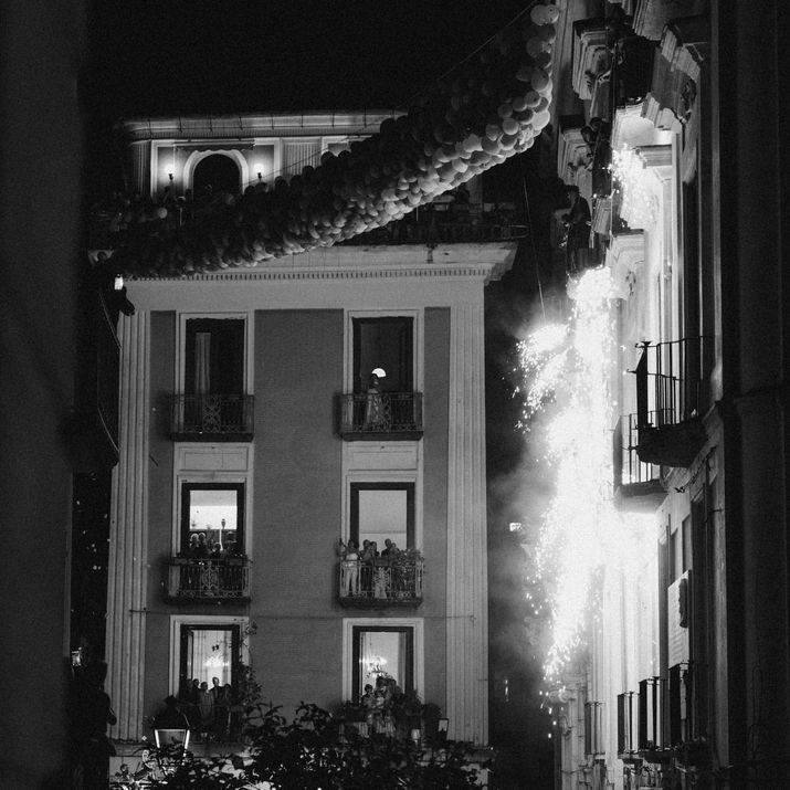 Black and white night photograph of a historic building decorated with lights and festive garlands hanging across the street.