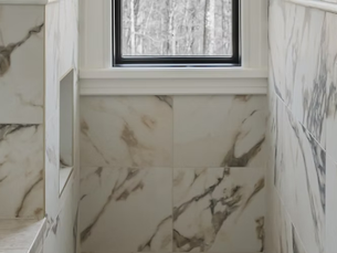 Close-up of a modern tiled bathroom or shower area featuring marble-patterned wall tiles, a built-in niche shelf, and a small window letting in natural light.