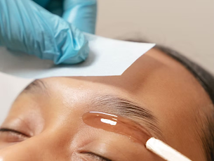 Esthetician wearing blue gloves applies cream above a client’s eyebrow during a facial treatment.